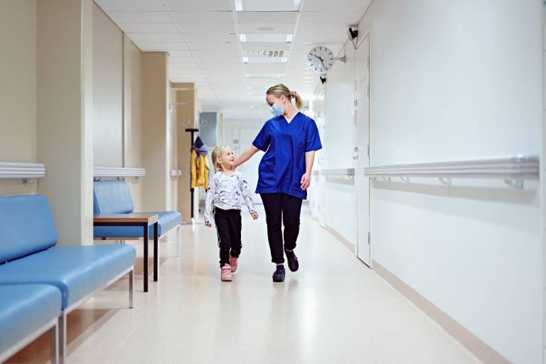 Sairaanhoitaja kävelee lapsen kanssa käytävällä.