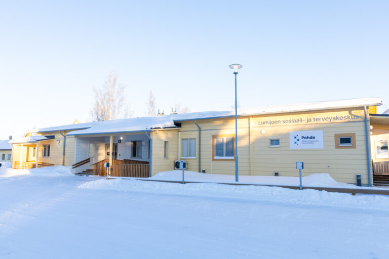 Vaaleankeltainen rakennus aurinkoisella pakkassäällä. Lunta maassa ja sininen taivas.