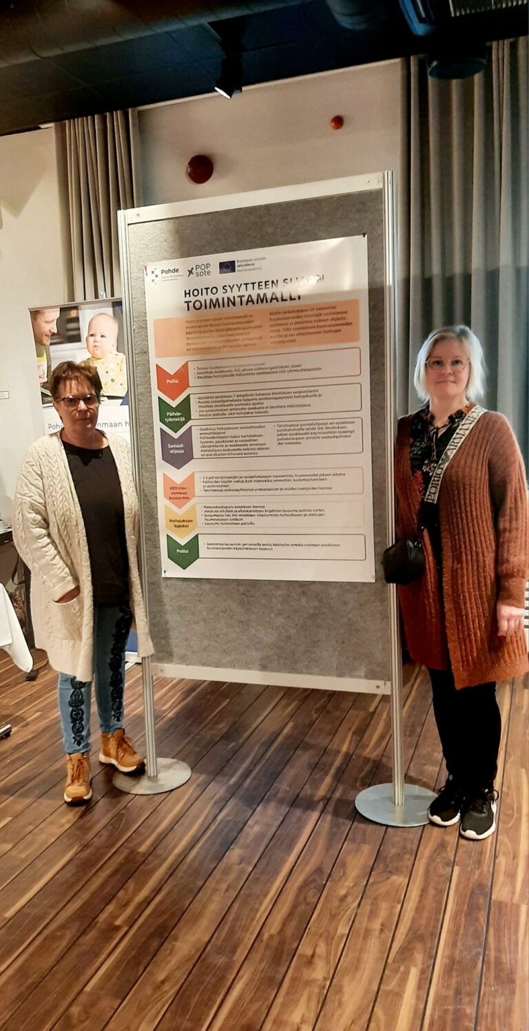 Nina Seppänen ja Päivi Rytinti seisomassa Hoito syytteen sijaan -toimintamallia esittelevän posterin vieressä