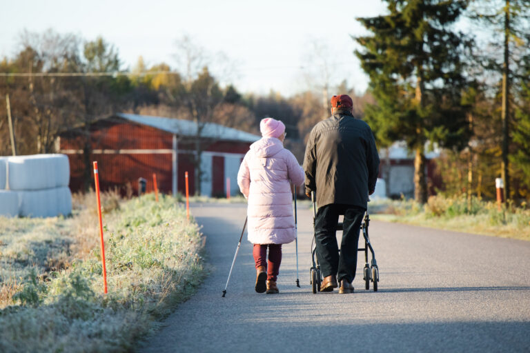 Kaksi ikäihmistä syysmaisemassa kävelyllä.