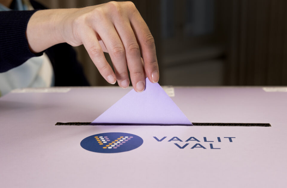 Käsi tiputtaa valkoisen lomakkeen laatikkoon, jossa lukee vaalit.