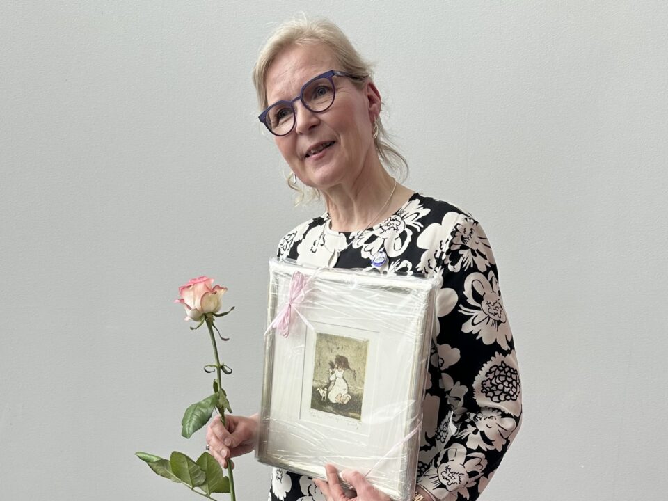 Nainen pitelee kädessään palkintoruusua ja taulua.