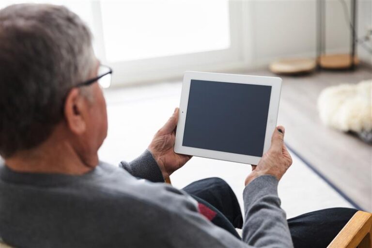 Iäkäs mies pitää kädessään tablettia.