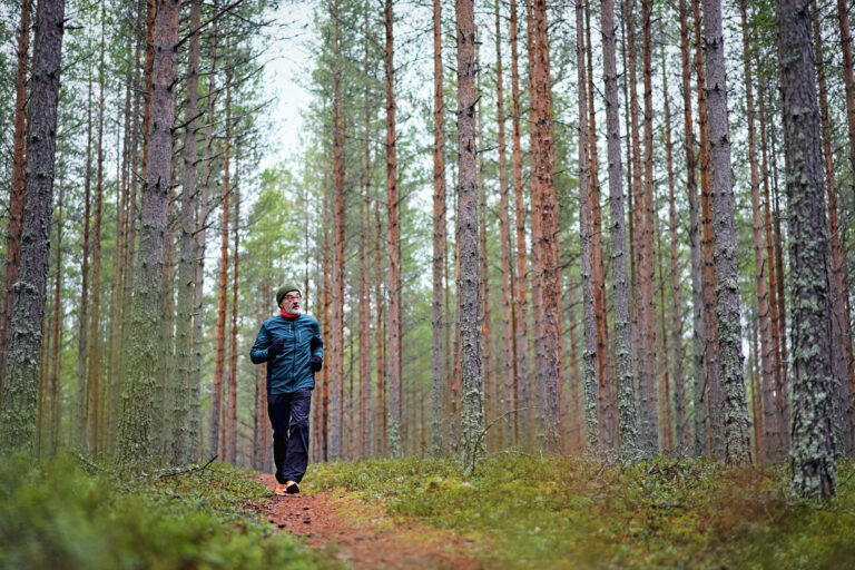 Iäkkäämpi mies juoksulenkillä metsäpolulla.