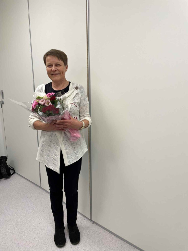 Nainen katsoo kameraa ja hymyilee.